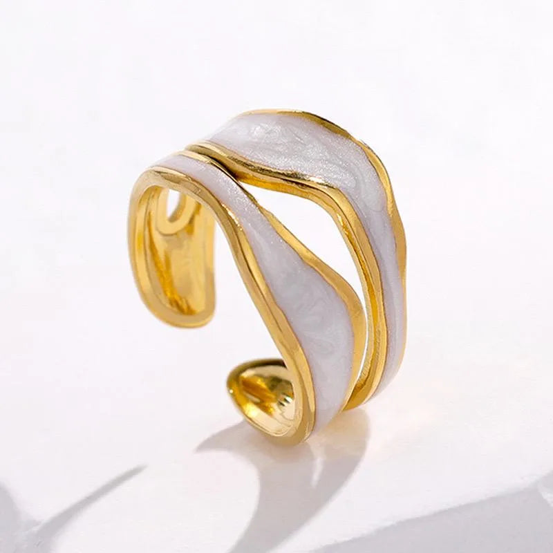 Gold and white wave-patterned ring on a reflective surface with a light gray background